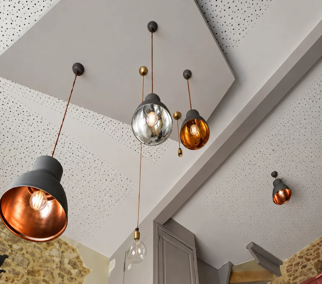 Suspensions cuivrées et miroir sous le plafond acoustique, entre les murs de pierre