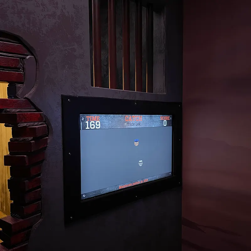 Une cellule terminée : écran de jeu encastré dans un mur sombre, à côté d’une ouverture en briques