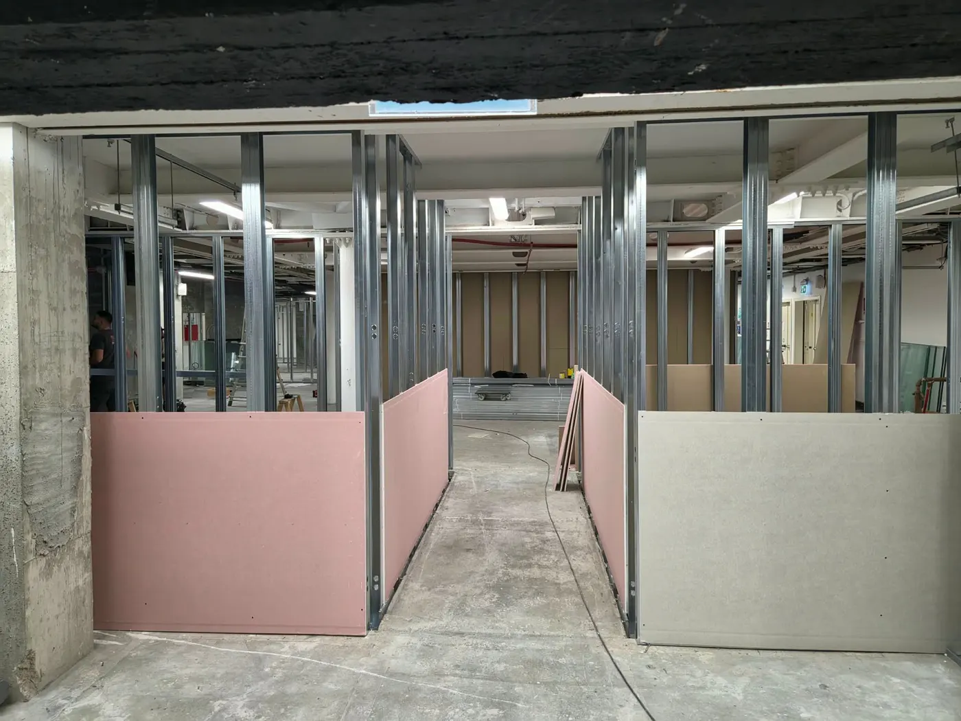 Chantier : cellules en cours de cloisonnement, plaques de plâtre posées à mi-hauteur de part et d’autre d’une circulation