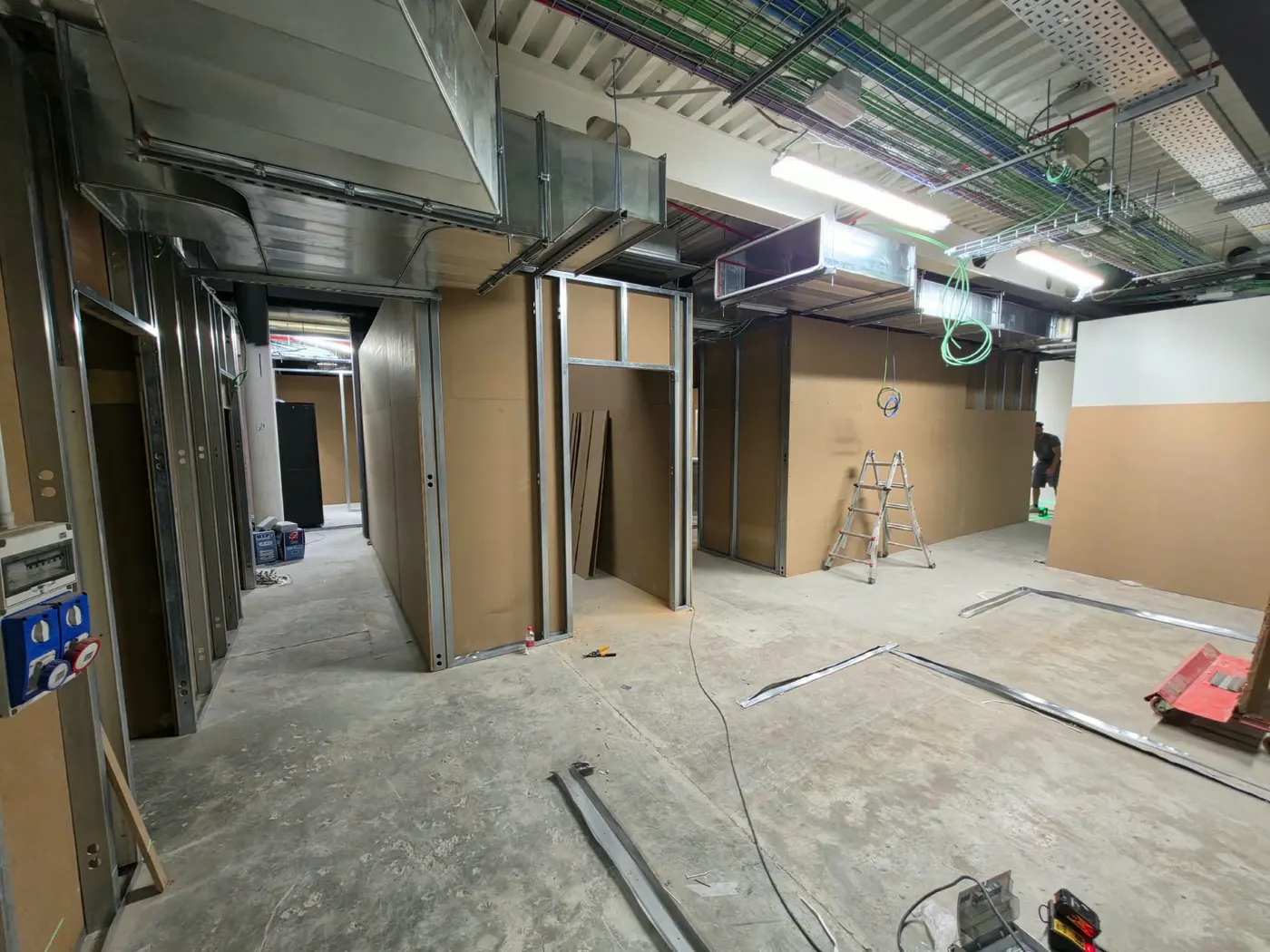 Chantier : couloir bordé de cloisons et d’encadrements de portes, gaines techniques au plafond