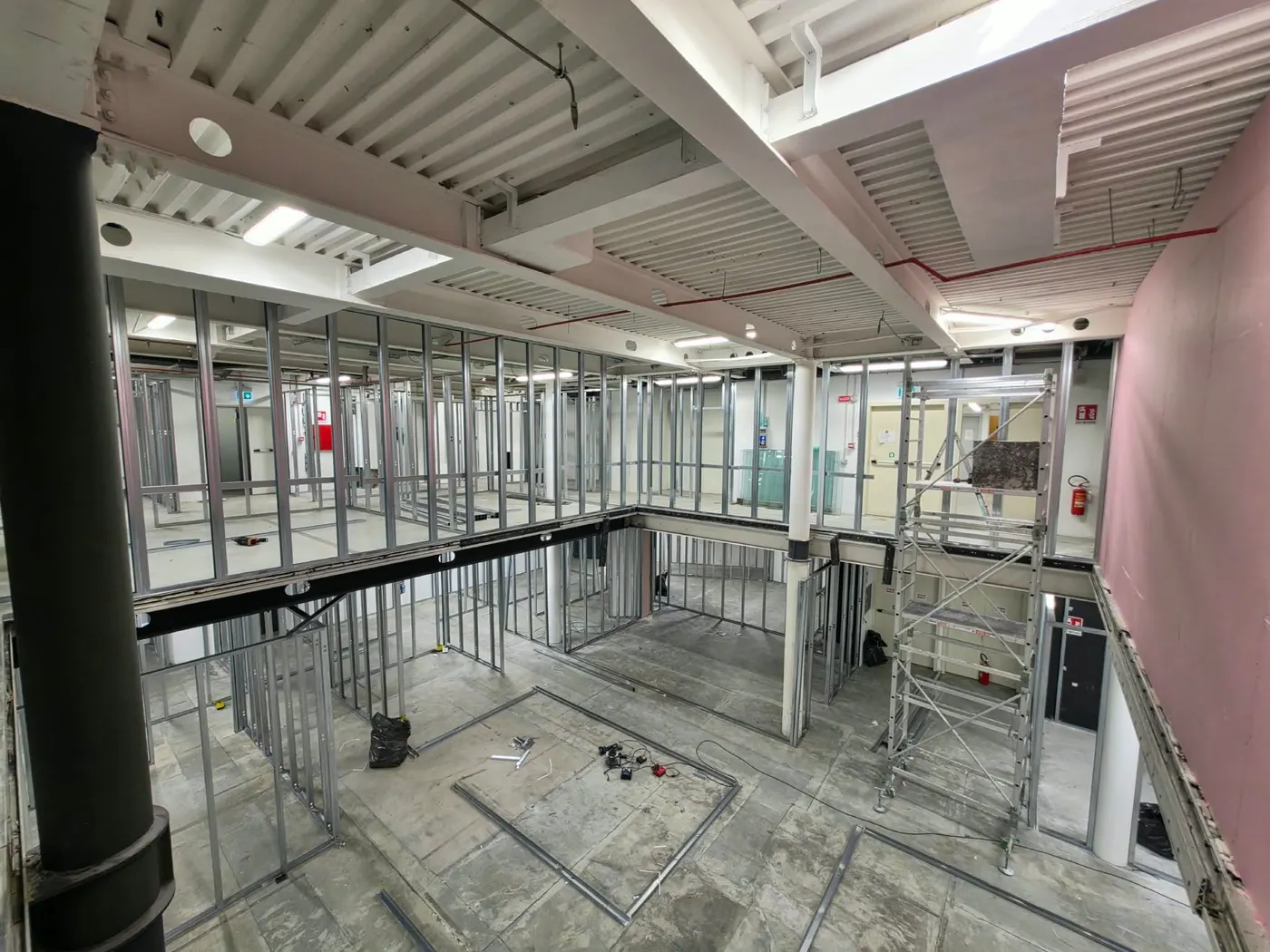 Chantier : ossatures métalliques des cloisons en cours de montage, sous un volume en double hauteur aux murs roses