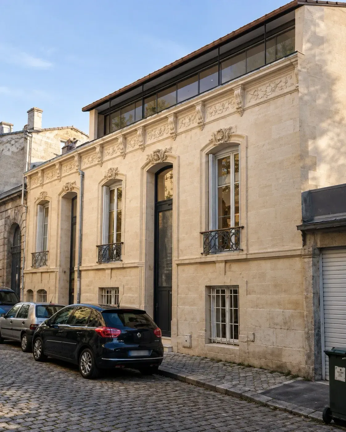 Échoppe en pierre calcaire sur une rue pavée de Bordeaux, surélevée d’un étage vitré en retrait sous un toit de tuiles