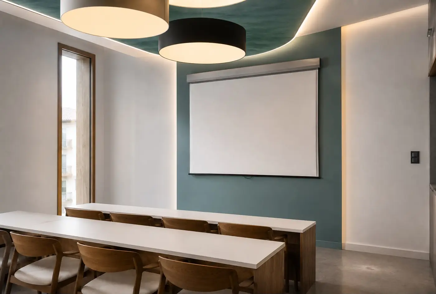 Perspective d’une salle de cours : longues tables en bois face à un écran de projection, mur vert grisé et grandes suspensions