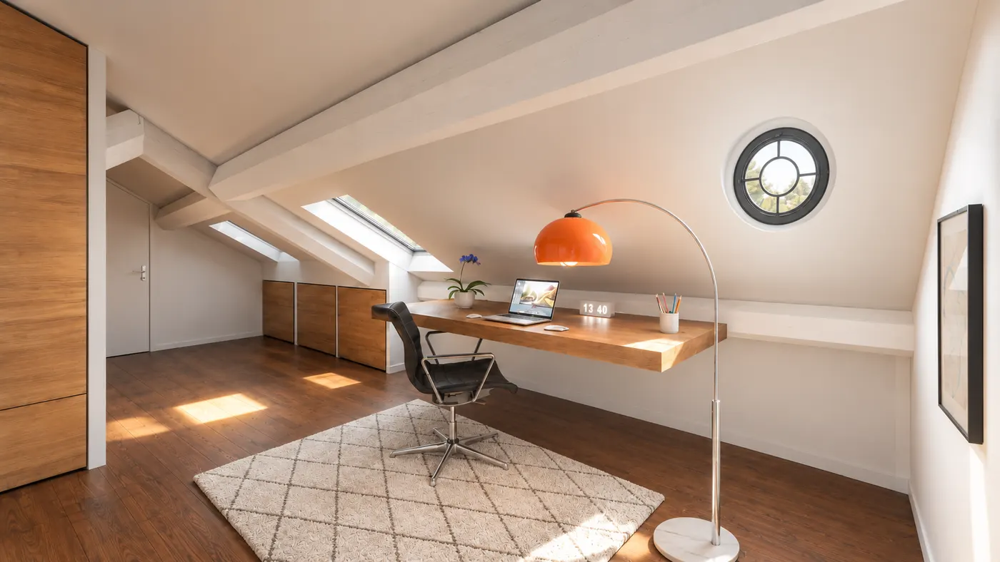 Perspective d’un espace bureau sous la charpente&nbsp;: plan de travail en bois, fenêtre ronde, rangements bas sous les rampants