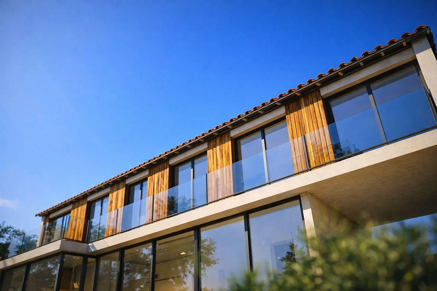 Maison aux Angles en contre-plongée : façade à bardage bois vertical, garde-corps vitrés et toit de tuiles sous un ciel bleu