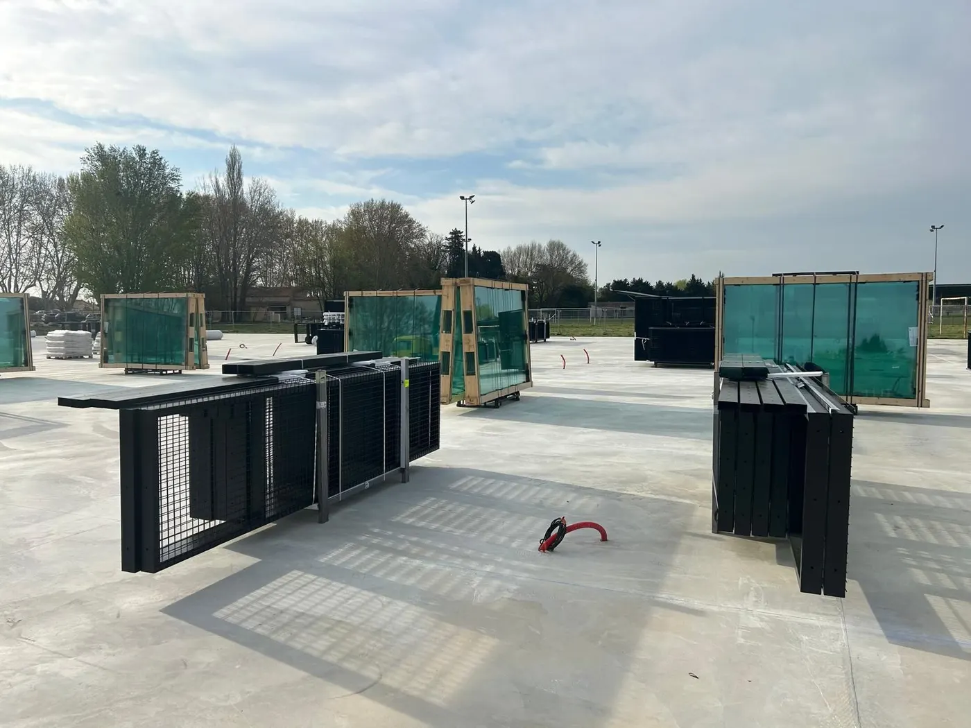 Chantier : panneaux vitrés et grilles des terrains posés sur la dalle en béton, avant montage